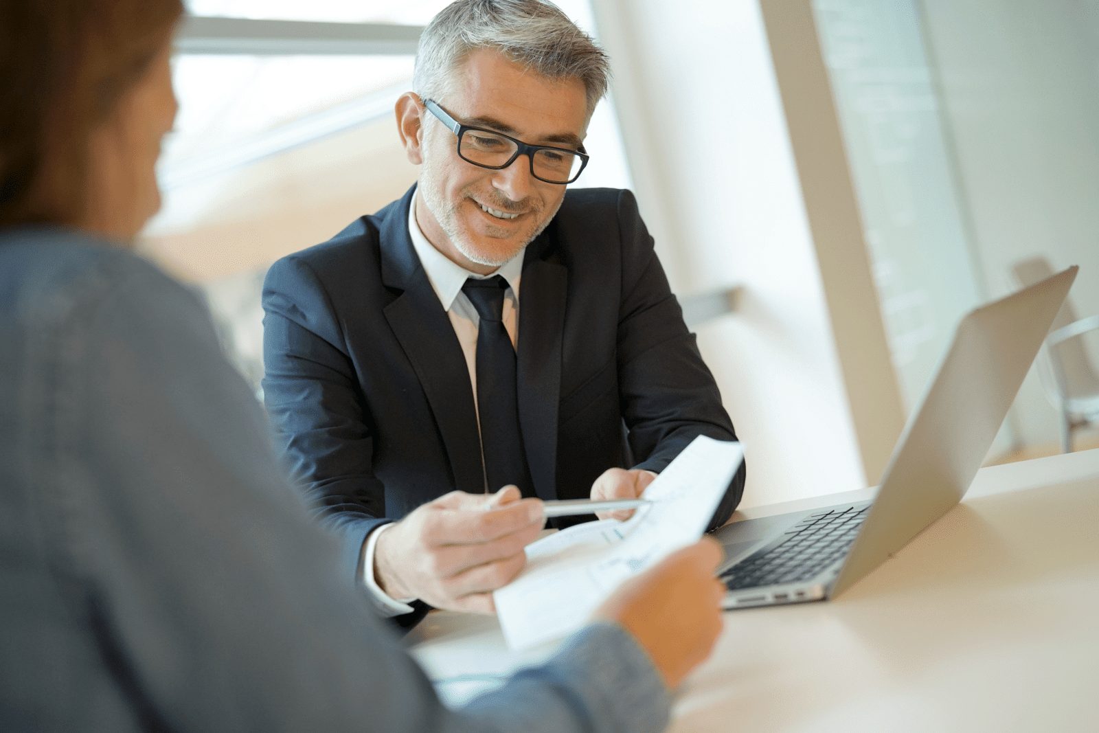 Man at computer pointing at paperwork with a pen