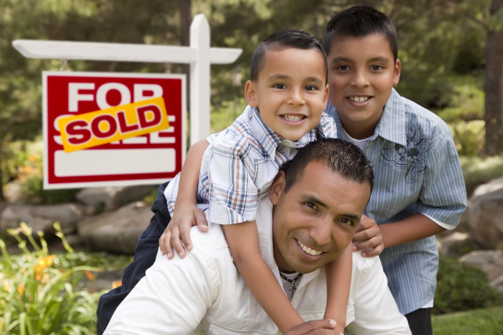Man and his children in front of a sold sign for their new home.