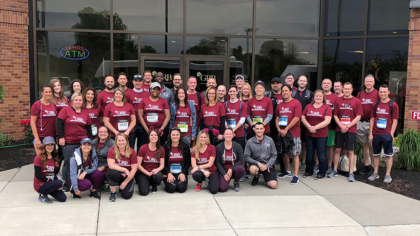 big group of Genesee regional bank employees posing for a photo together outside brick building wearing red GRB shirts.